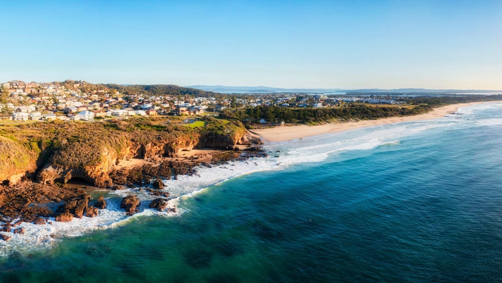 A coastal town with a beach, rocky cliffs, and a clear view of the ocean.
