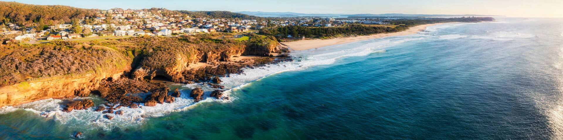 A coastal town with a beach, rocky cliffs, and a clear view of the ocean.
