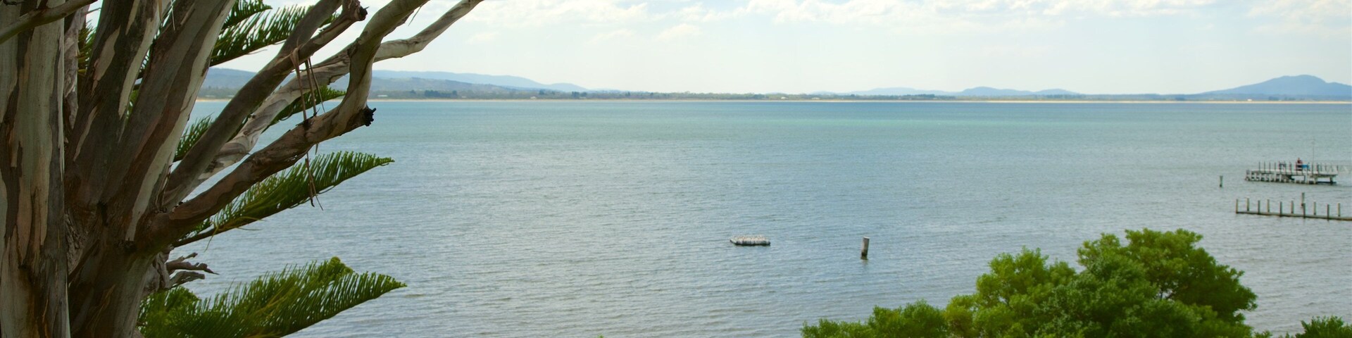 A calm lake with a pier, surrounded by trees and a distant mountain range.