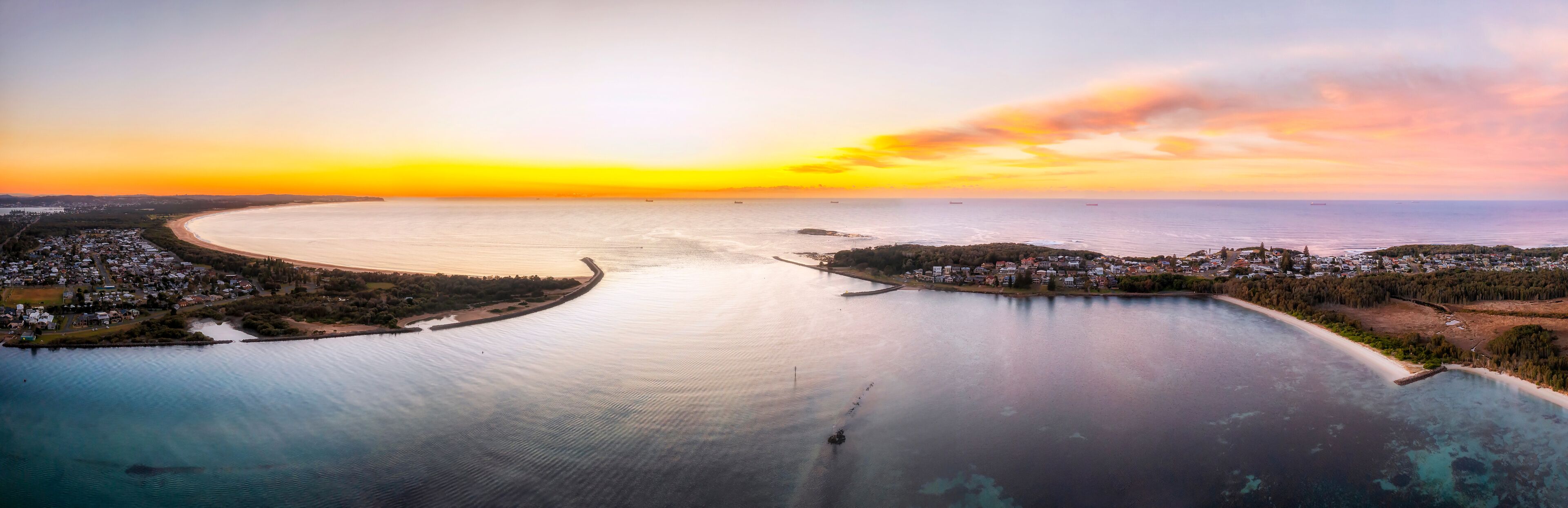 A coastal town with a large bay, a marina, and a sunset over the water.