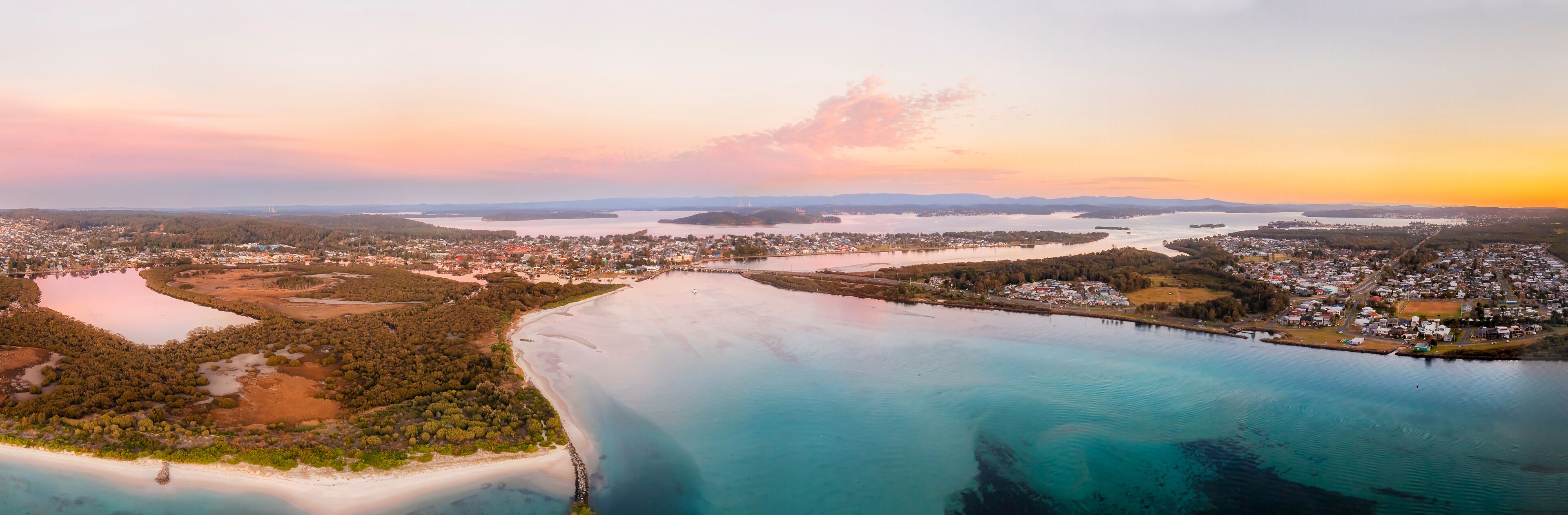 An aerial view of a coastal town with a large bay, surrounded by forests and islands.