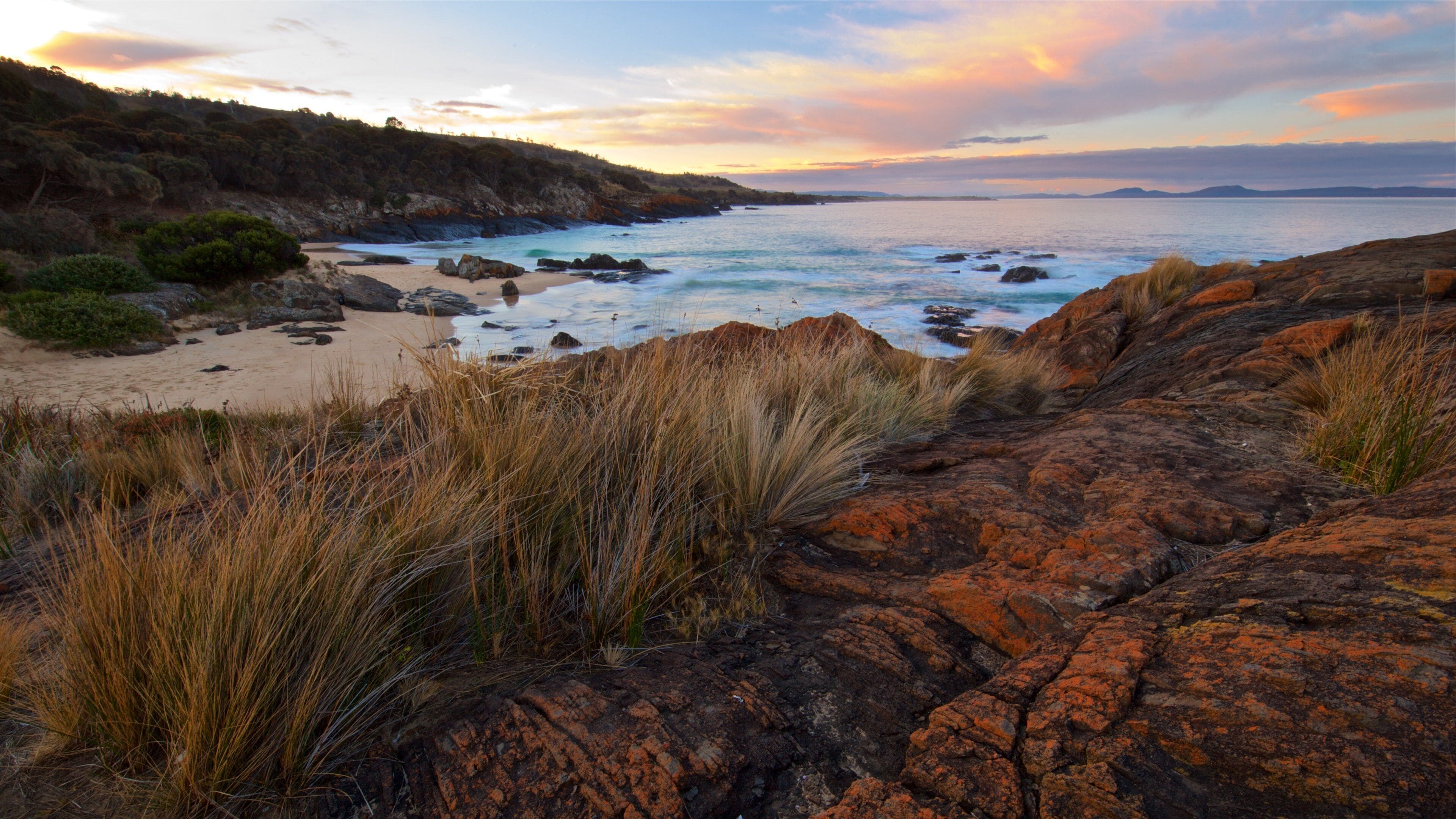A coastal landscape with rocky outcrops, sandy beach, and grassy dunes.