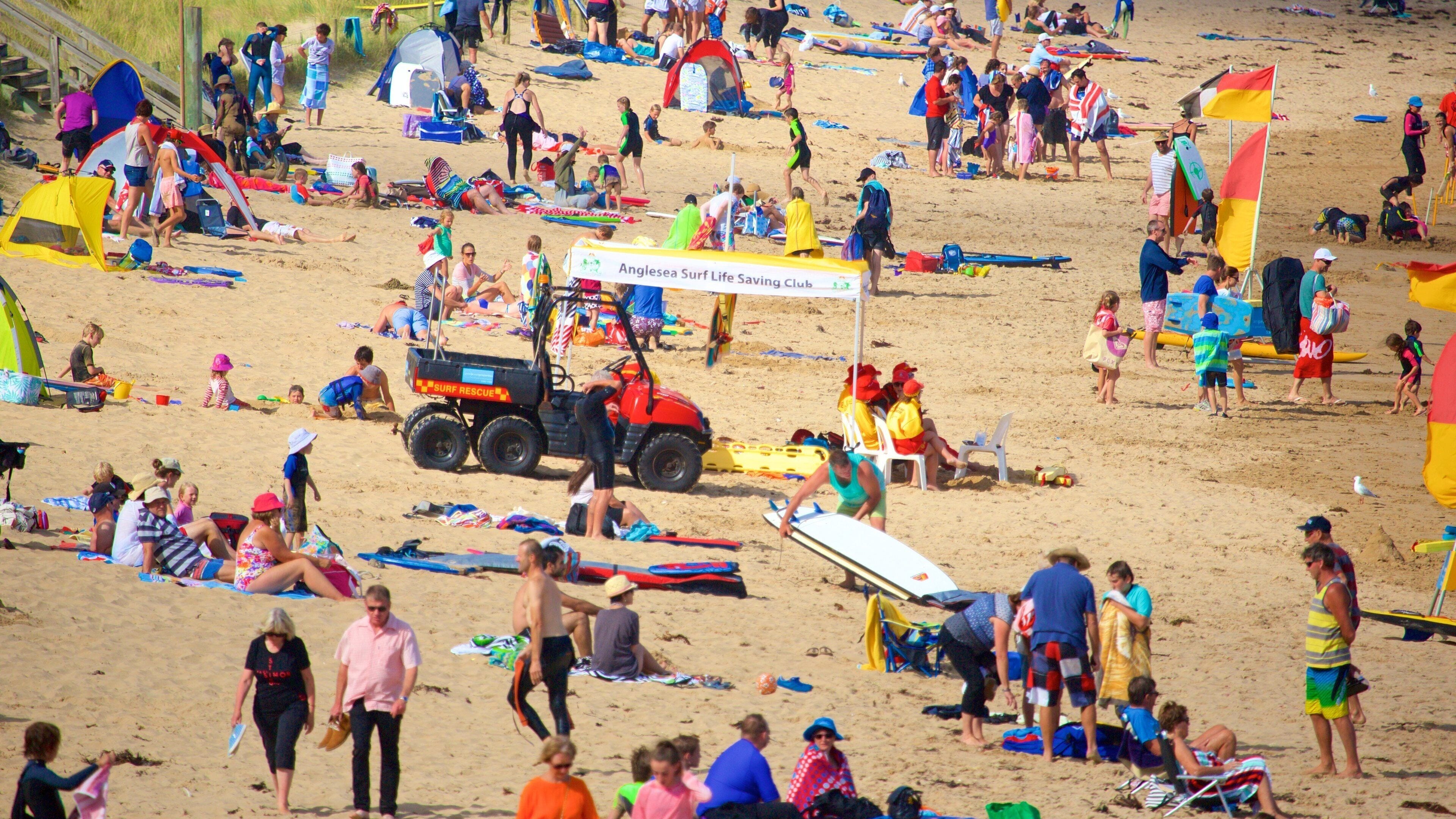 A crowded beach with tents, beach chairs, and a surf rescue vehicle.