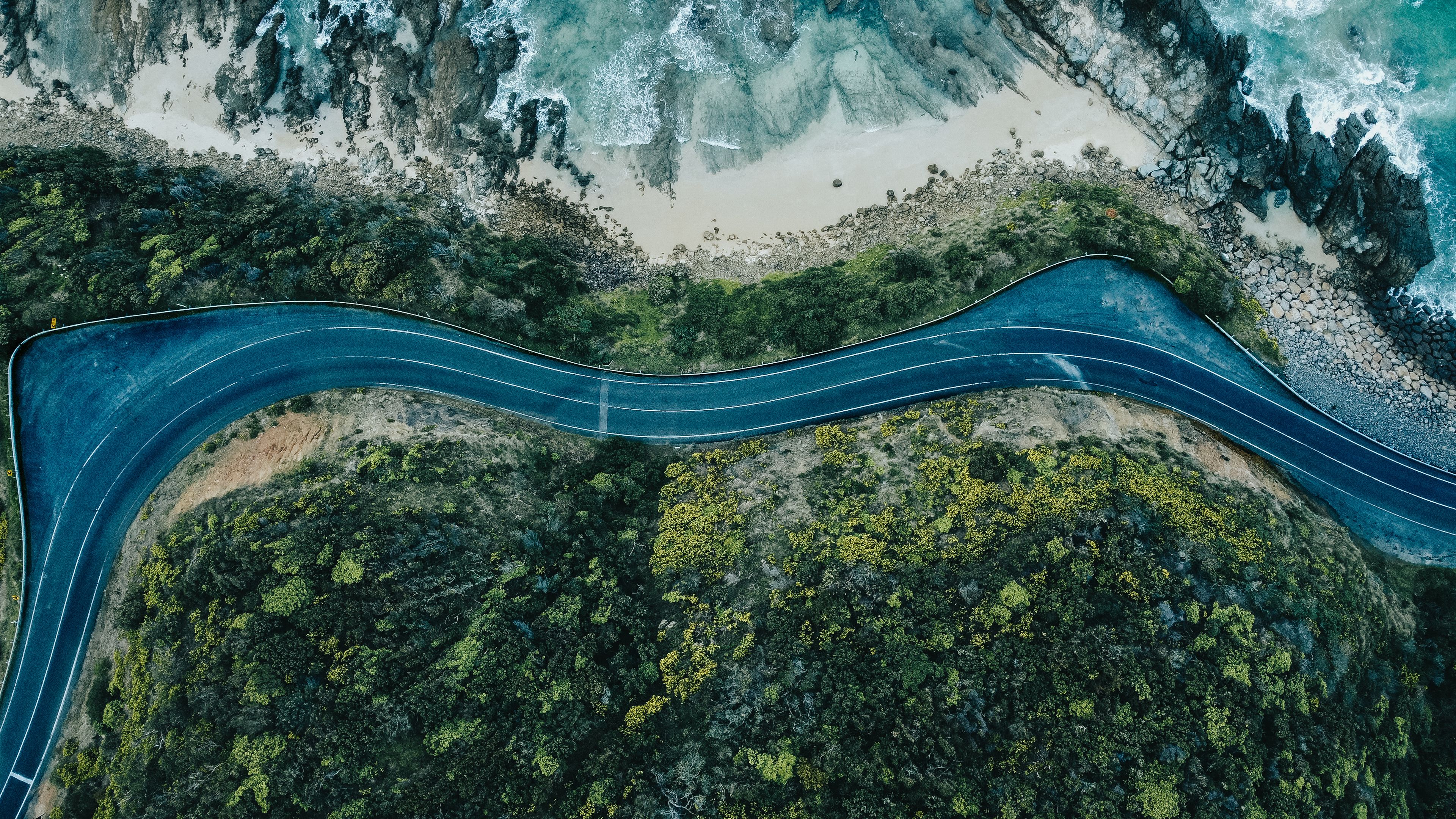 A winding road through a coastal area with rocky cliffs and dense green vegetation.