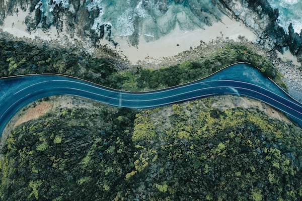 Eine kurvenreiche Straße schlängelt sich durch eine Küstenlandschaft mit schroffen Klippen und dichtem Grün.