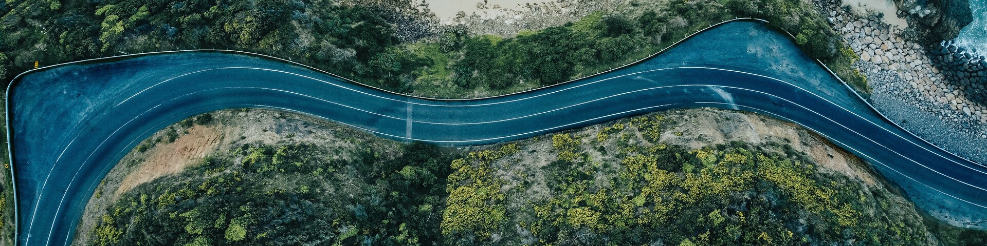 Eine kurvenreiche Straße schlängelt sich durch eine Küstenlandschaft mit schroffen Klippen und dichtem Grün.