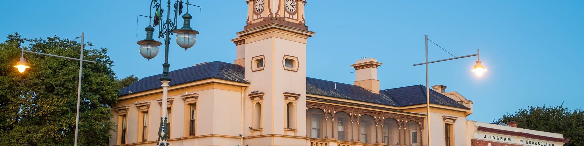 A historic post office with a clock tower, ornate architecture, and a street with benches and shops.