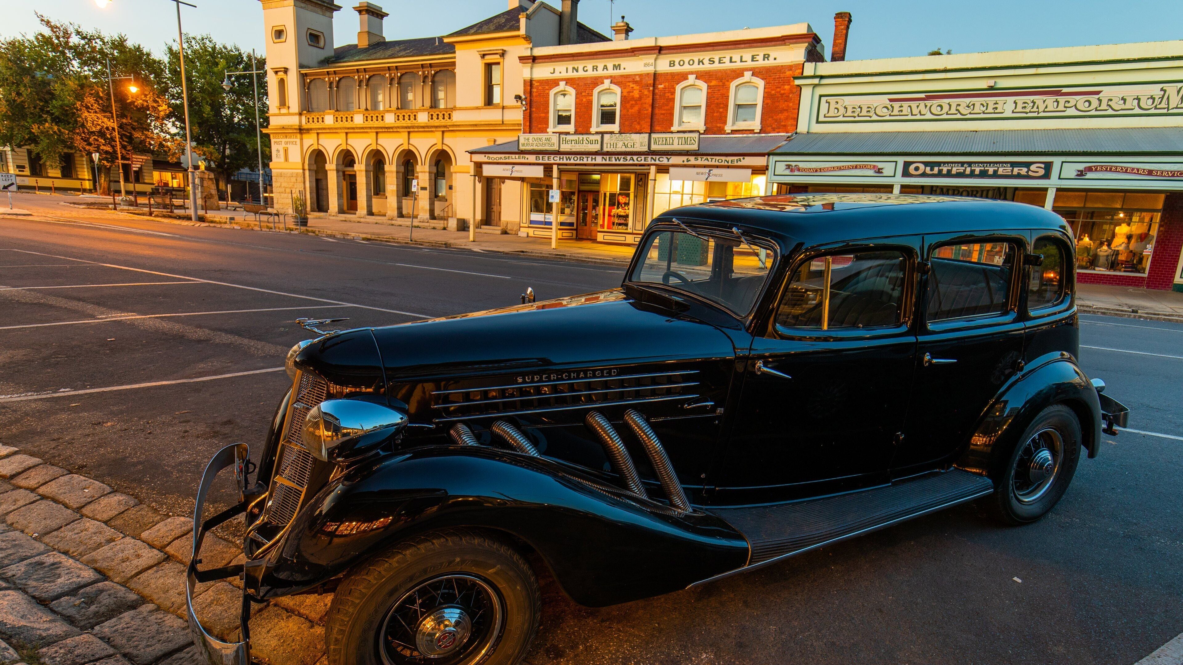 A vintage black car parked on a street with historic buildings in the background.