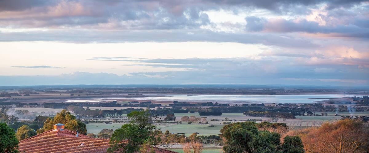 A rural landscape with fields, trees, and a distant body of water.