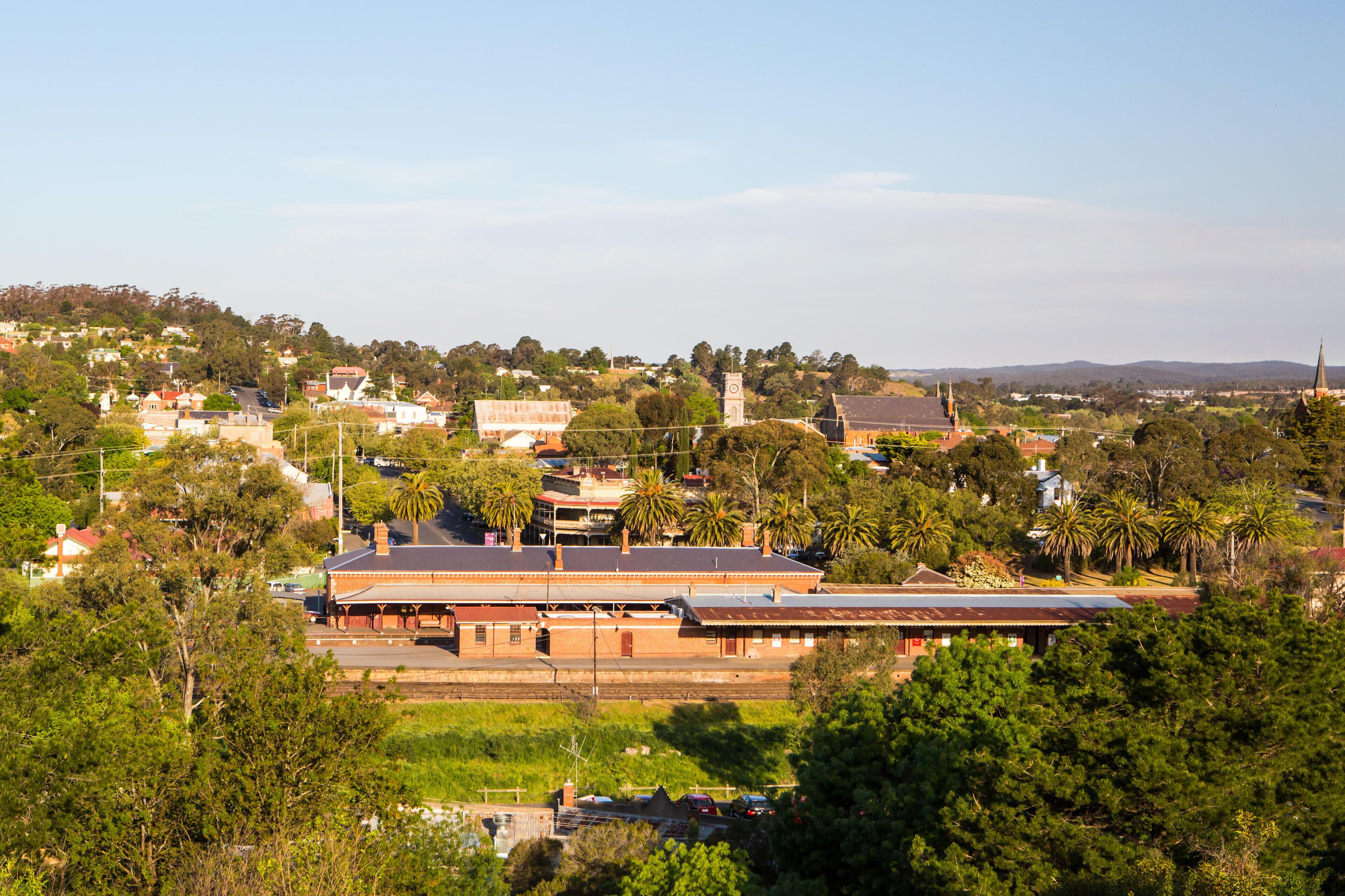 A railway station with a clock tower, surrounded by greenery and residential buildings.