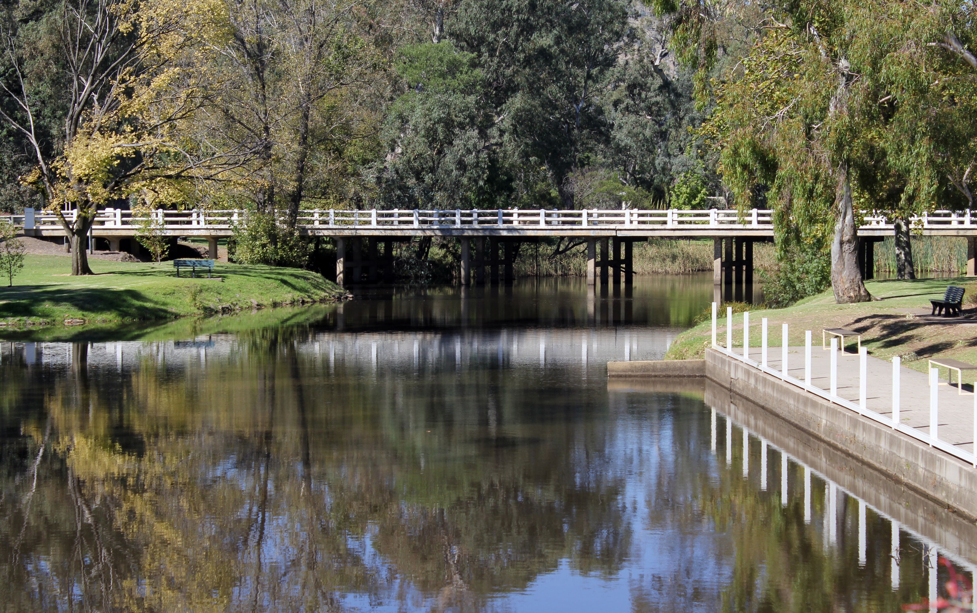 A calm river with a bridge and a park with benches.