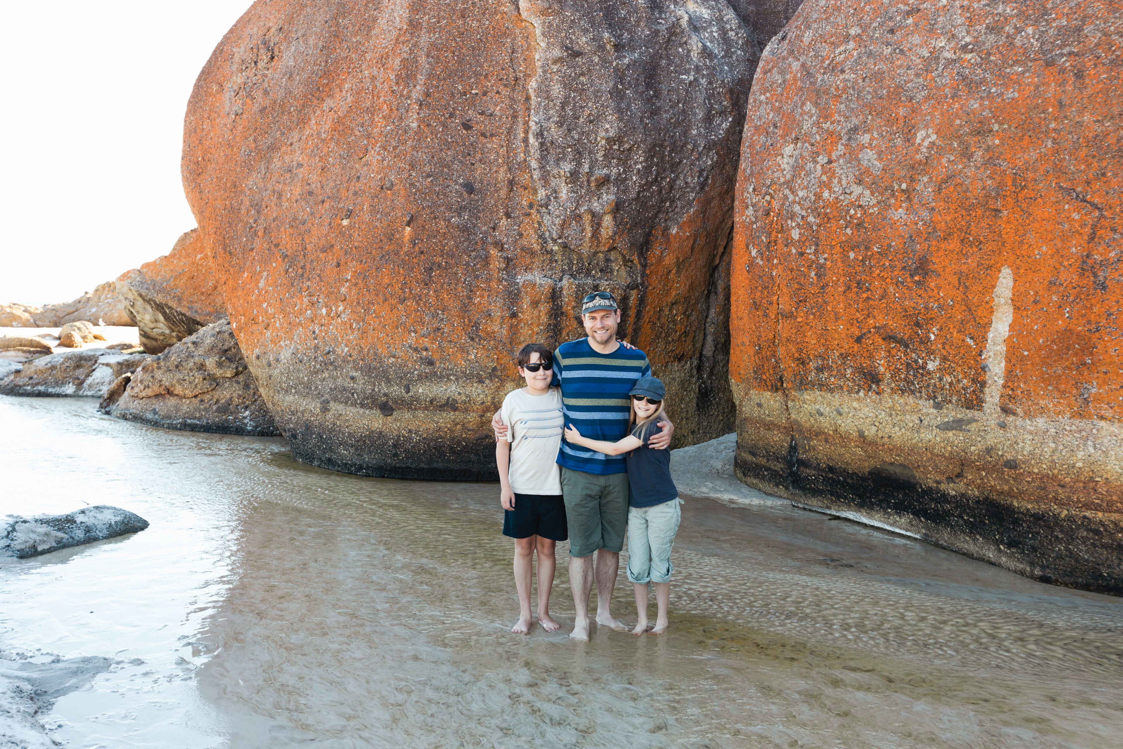a father, daughter and son wearing sun glasses and a hat next to boulder rocks at Squeaky beach in Wilson's Promontory South Gippsland Australia