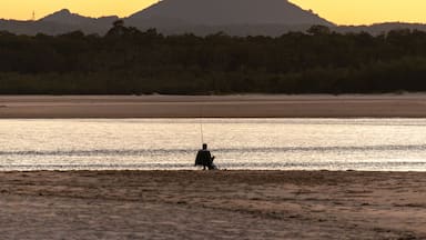 Rear View of Fisherman Sitting on the Beach at Sunset whit Mountain and Sea Landscape