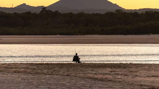 Rear View of Fisherman Sitting on the Beach at Sunset whit Mountain and Sea Landscape