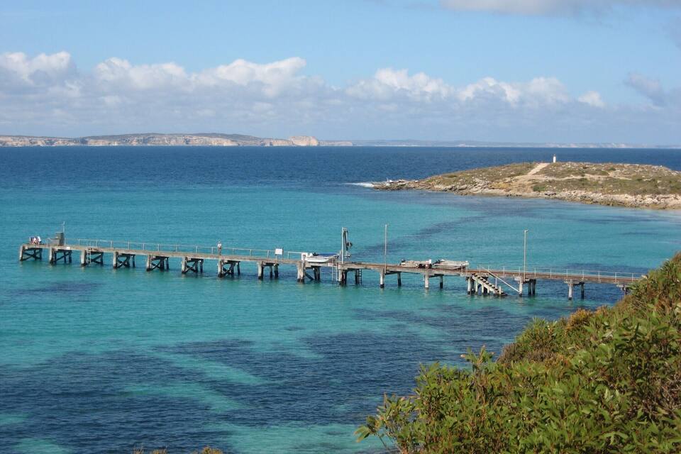 Un muelle se adentra en un mar turquesa, con una isla rocosa al fondo.