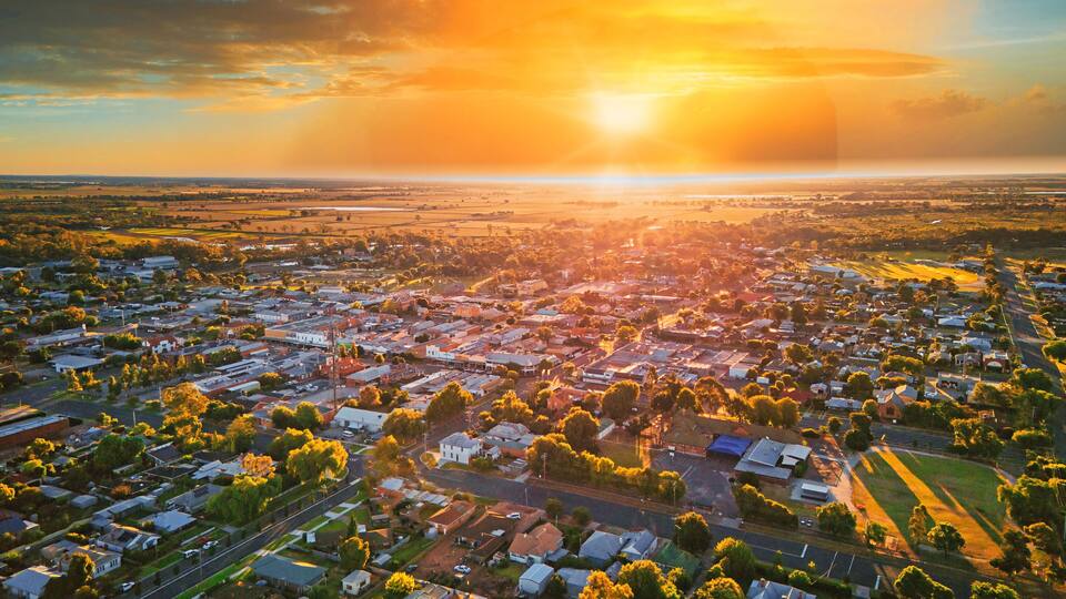 An aerial view of a town during sunset with a visible river and surrounding fields.