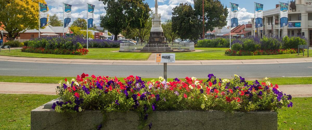Un parque con un monumento, coloridas camas de flores y un cielo azul despejado.