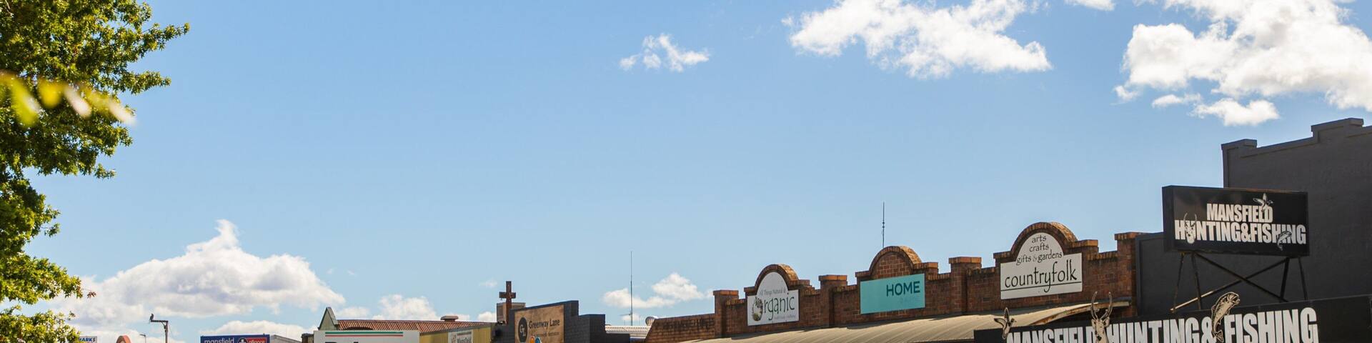 A busy street with various shops, including a bakery, a hunting and fishing store, and a country folk store.