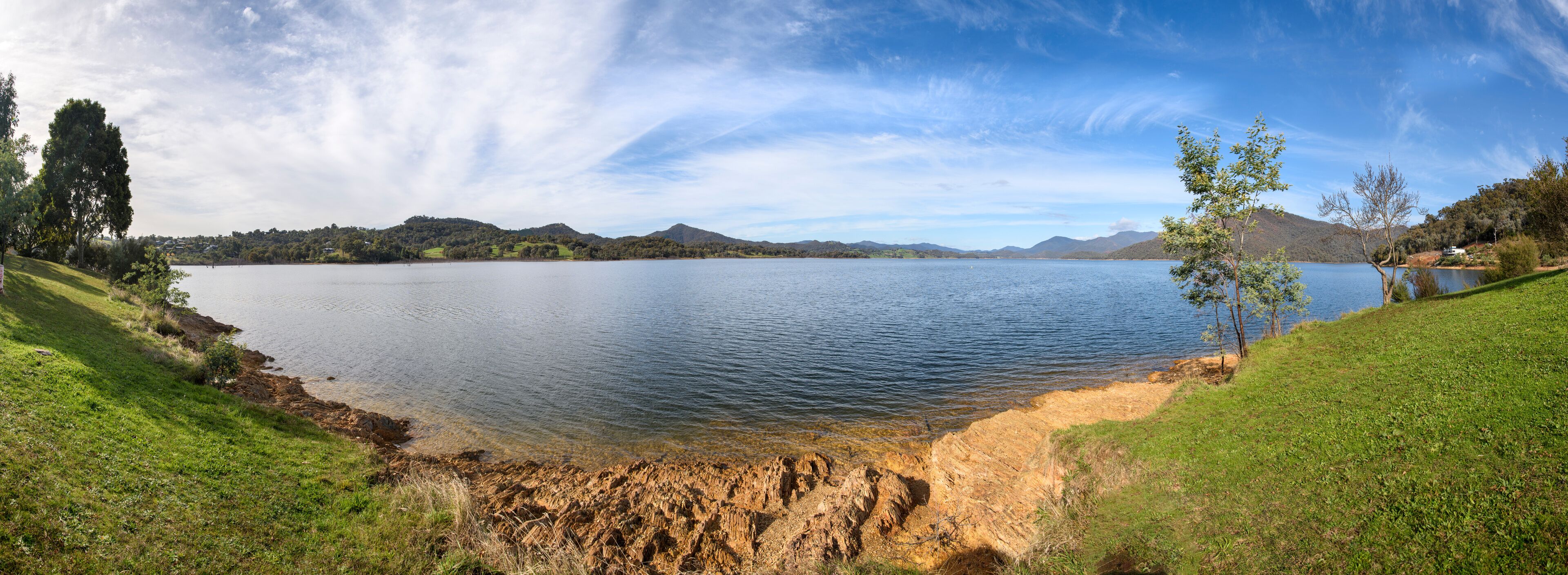 Un lago tranquilo rodeado de colinas verdes y un cielo despejado.