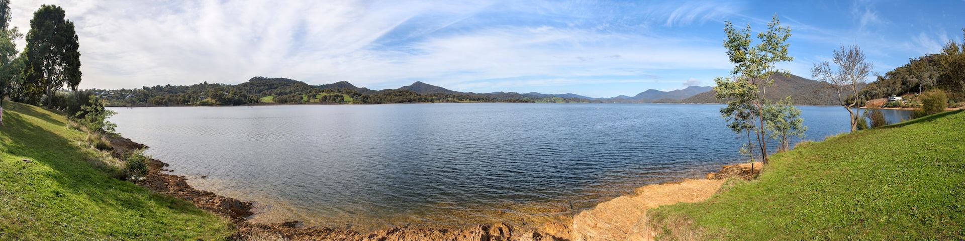 Un lago tranquilo rodeado de colinas verdes y un cielo despejado.