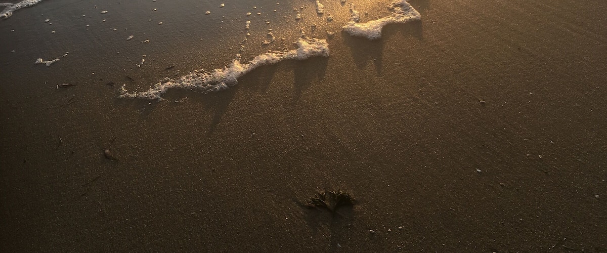 Reflection of the sun setting on the beach as the waves roll in slowly.