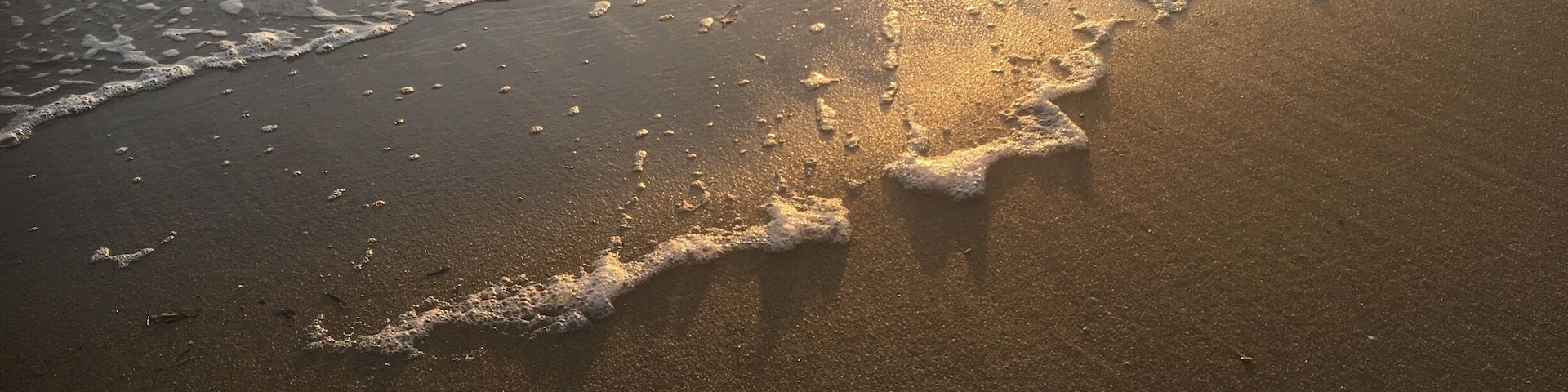 Reflection of the sun setting on the beach as the waves roll in slowly.