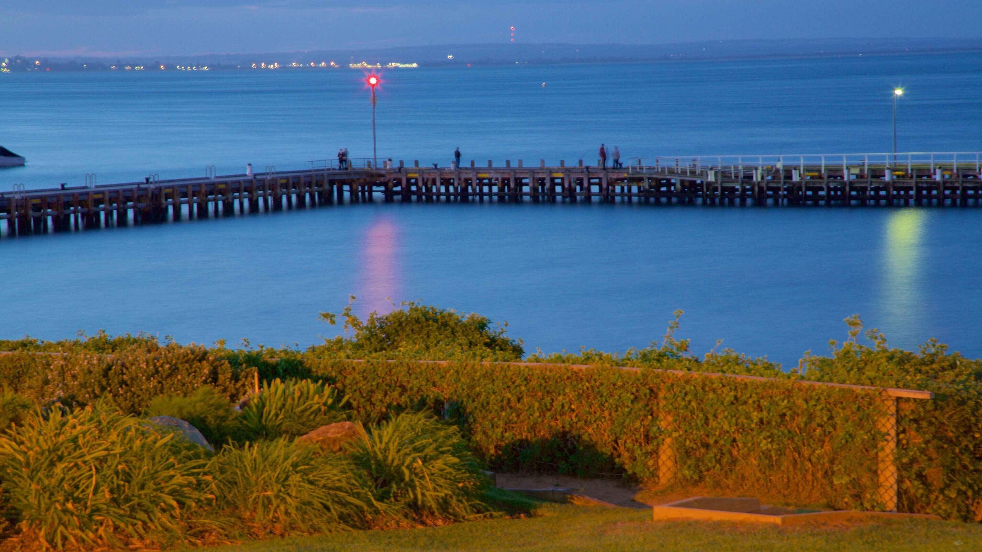 A pier extending into calm waters at dusk with distant city lights.