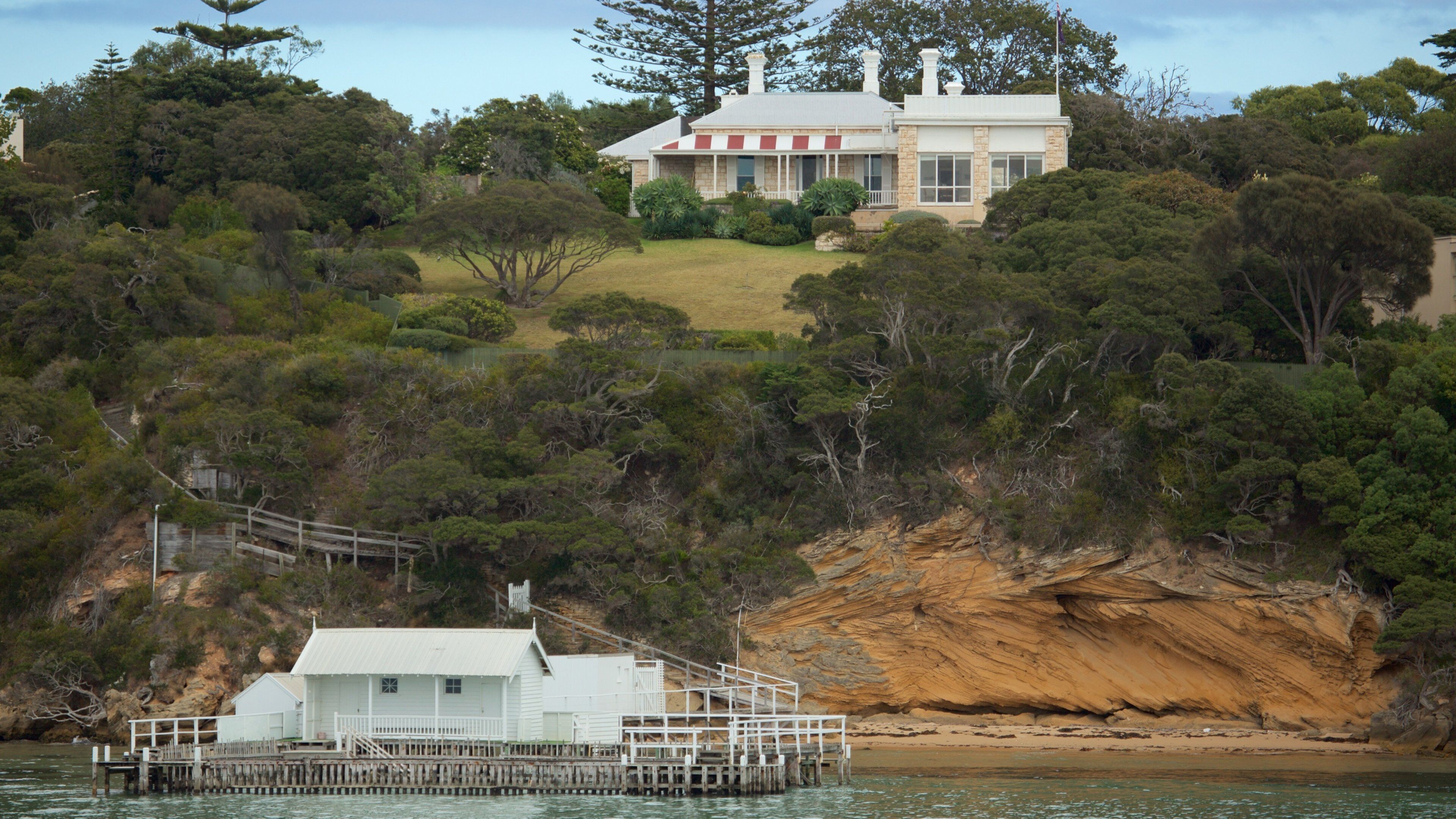 A coastal house surrounded by dense forest and a rocky cliff.