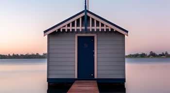 Ein kleines, hölzernes Bootshaus mit blauer Tür und weißer Umrandung, gelegen auf einem hölzernen Steg, der ins ruhige Wasser führt.