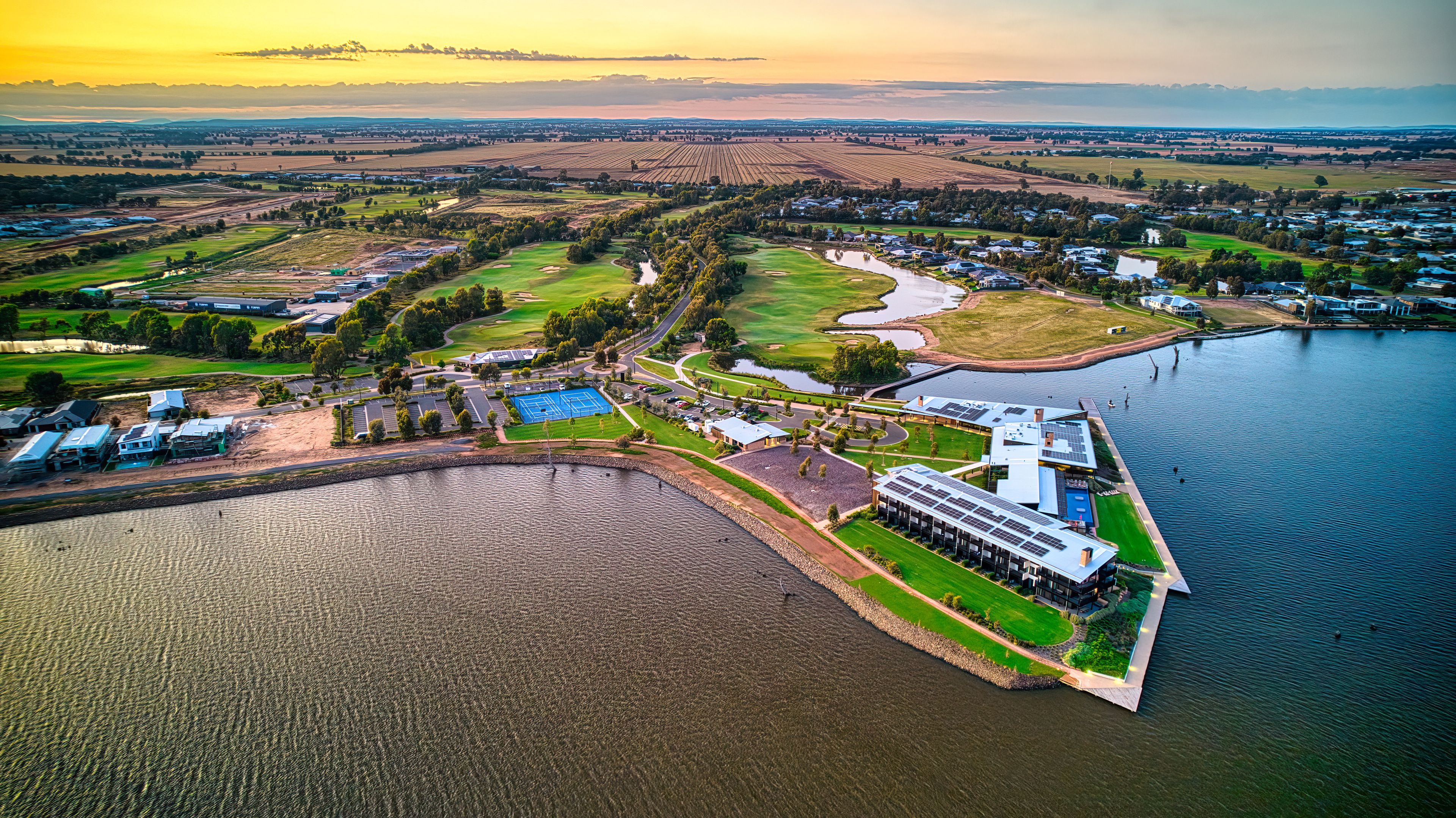 An aerial view of a lakeside community with residential areas, a golf course, and solar panels on buildings.