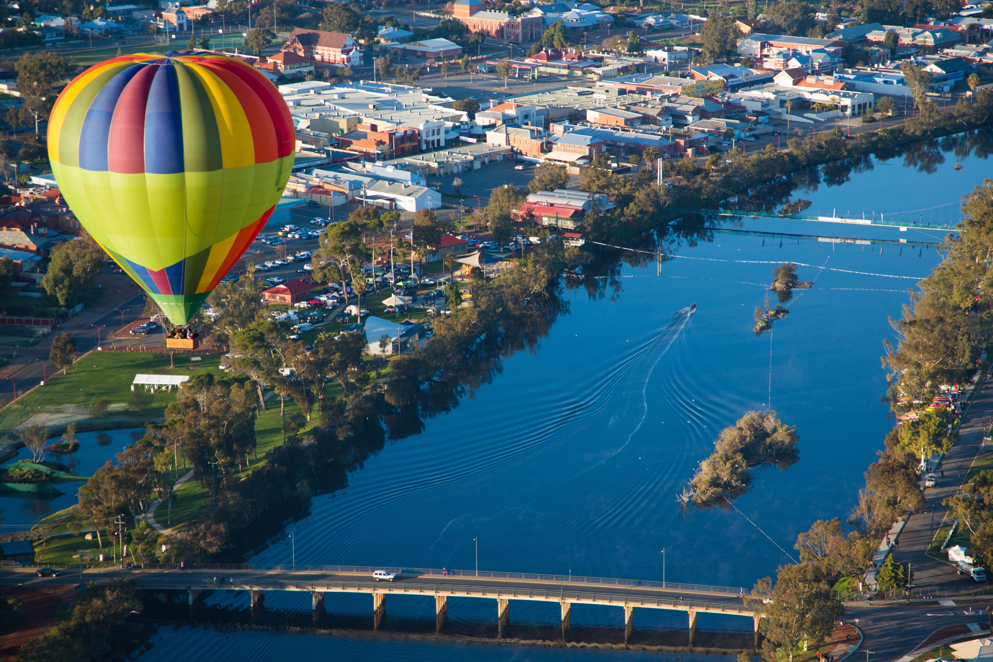 A hot air balloon over a river with a bridge and a town.