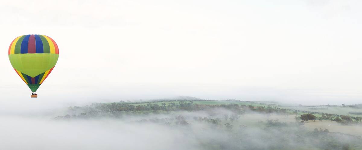 A hot air balloon flying over a misty landscape with green fields and trees.