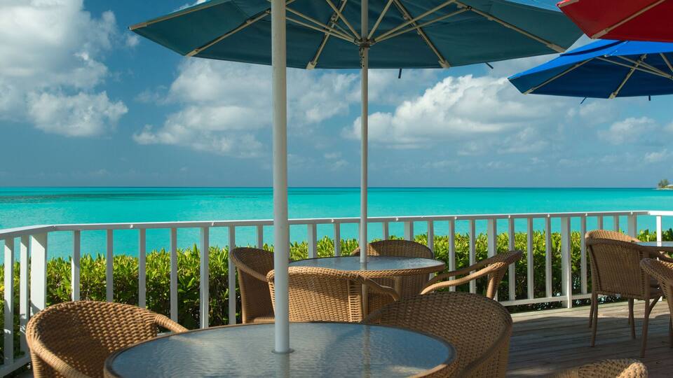 A deck with wicker chairs and tables overlooking turquoise waters.