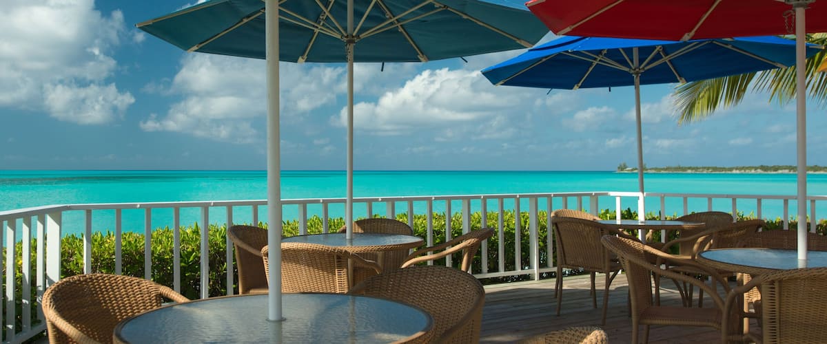 A deck with wicker chairs and tables overlooking turquoise waters.