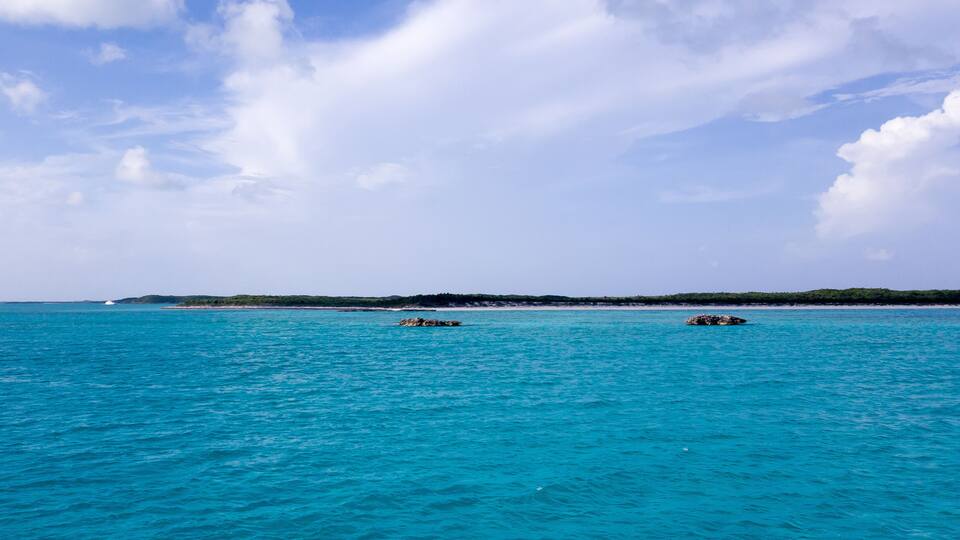 A turquoise sea with two small islands in the distance and a clear sky.
