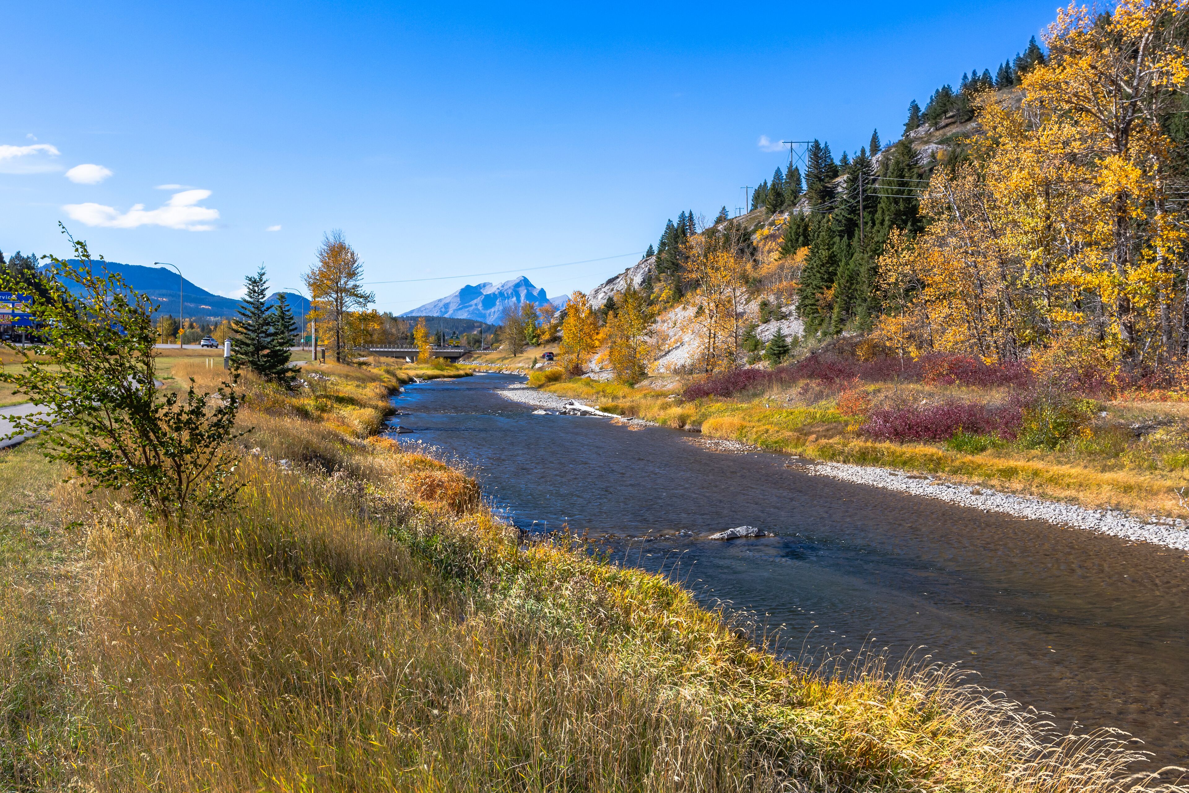 A river flowing through a mountainous area with autumn foliage and a bridge in the distance.