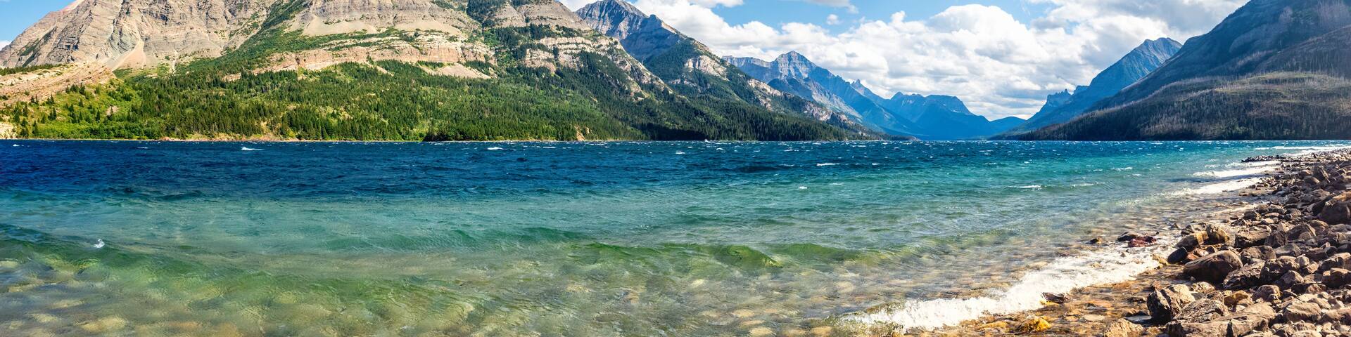 A mountain range, clear blue lake, and rocky shoreline.