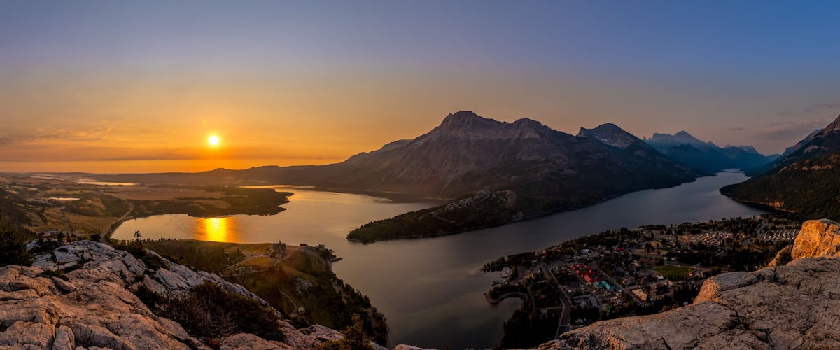 A mountainous landscape with a lake and a sunset.