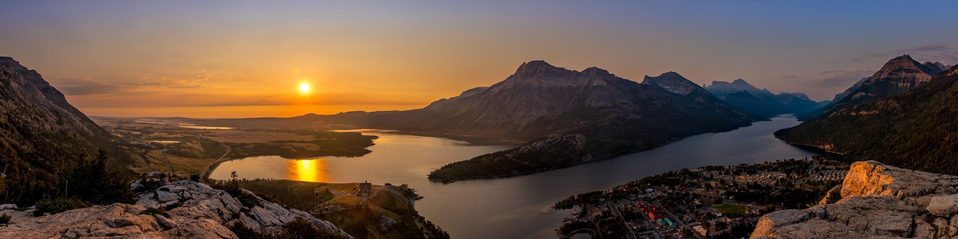 A mountainous landscape with a lake and a sunset.