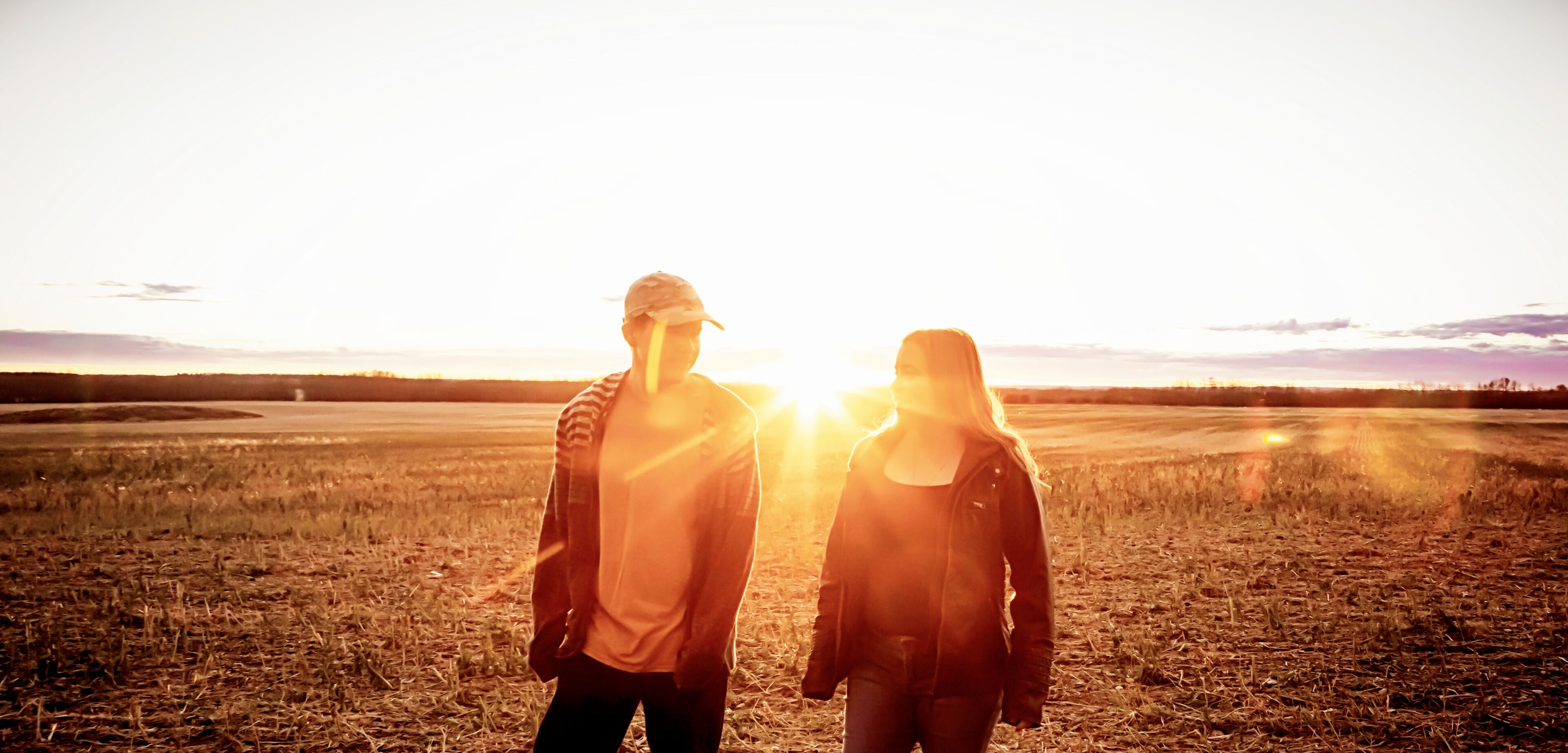 Two people standing in a field with the sun low on the horizon.