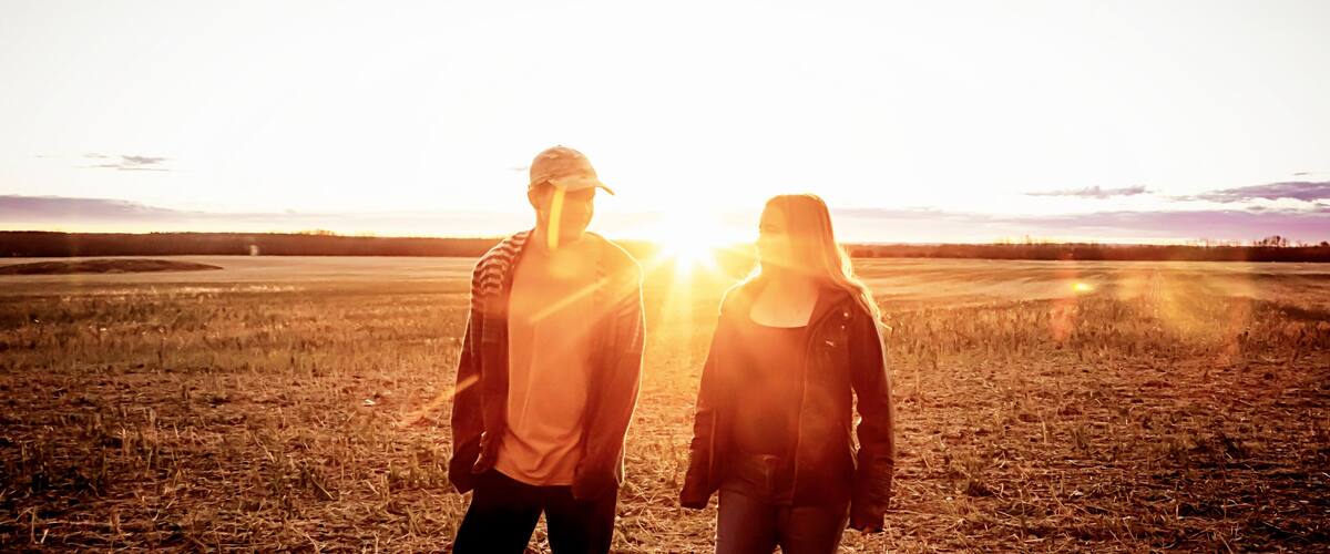 Two people standing in a field with the sun low on the horizon.