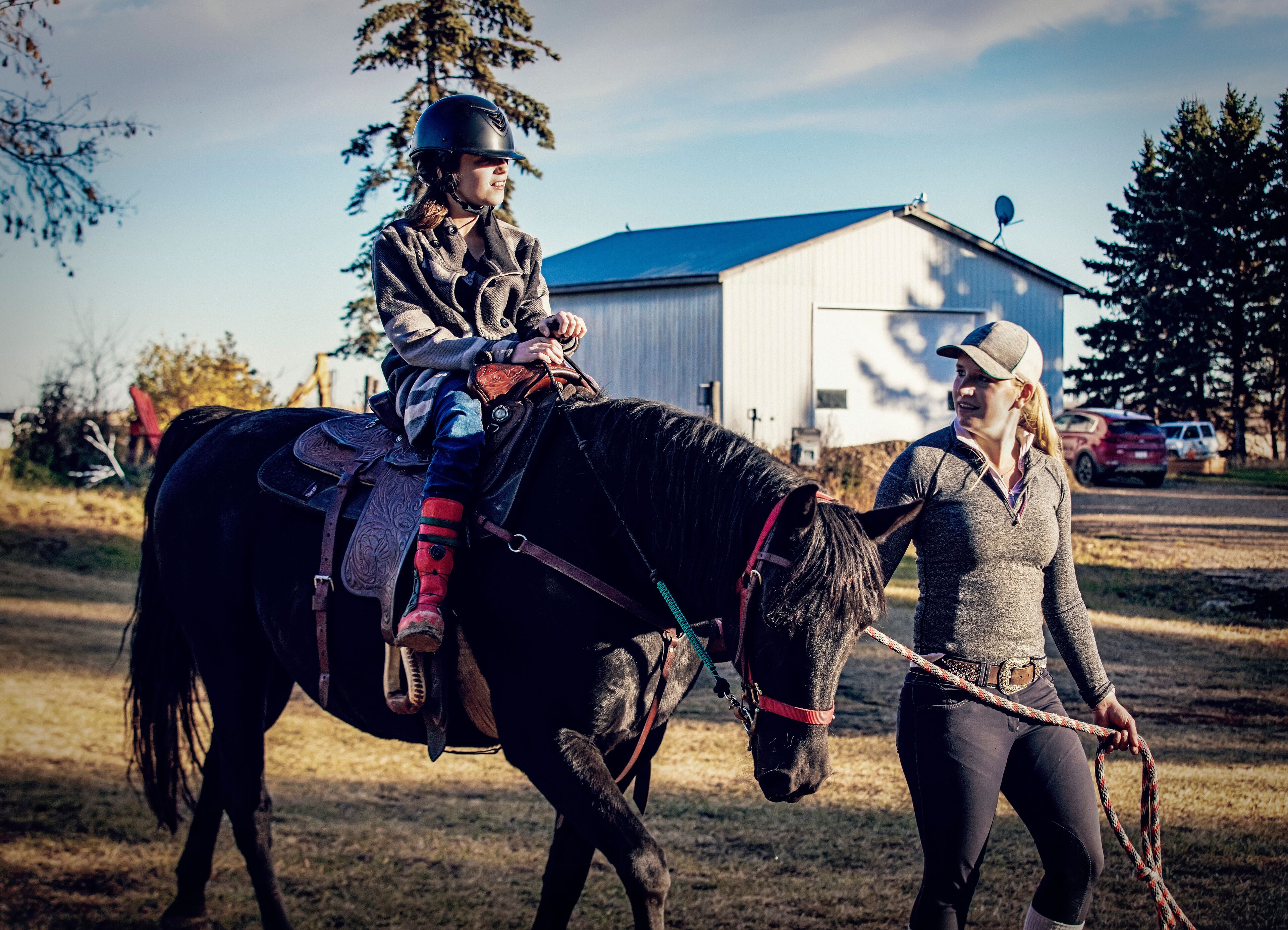 A young girl with Cerebral Palsy and her trainer working with a horse during a Hippotherapy session; Westlock, Alberta, Canada