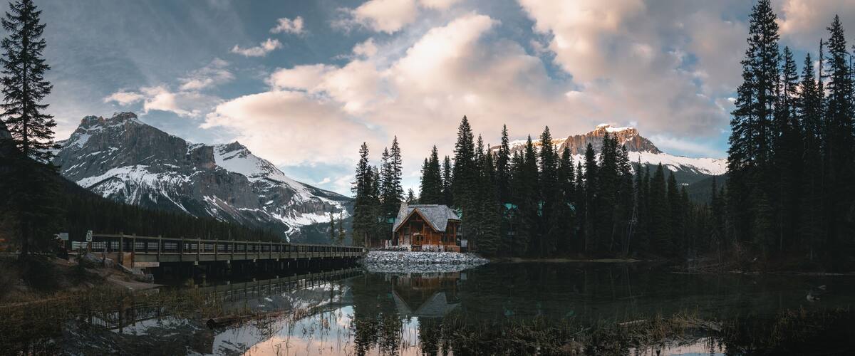A cabin by a lake with mountains in the background.