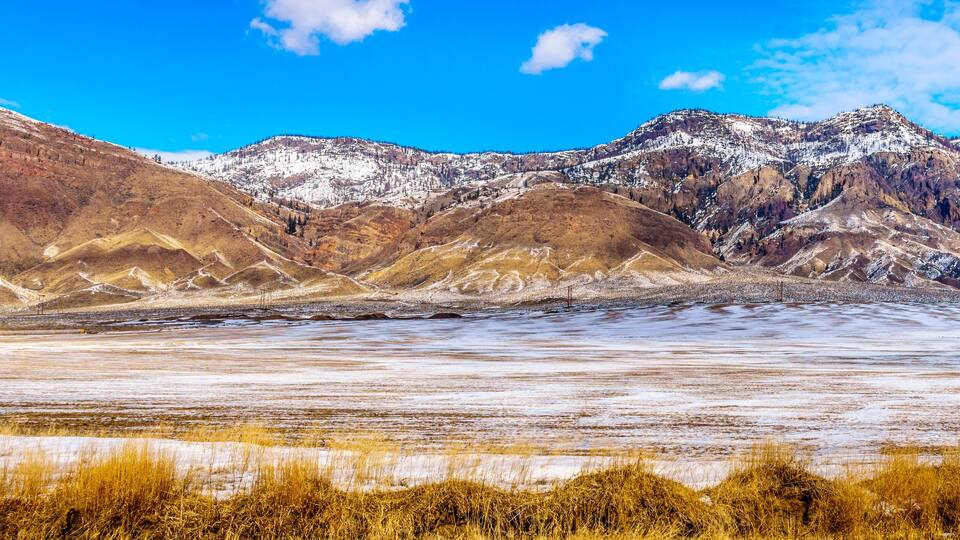 A mountainous landscape with snow-covered peaks and a flat valley.