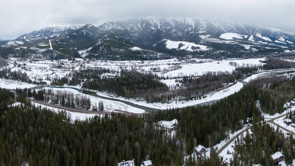 A snow-covered mountainous landscape with a river winding through a forested valley.
