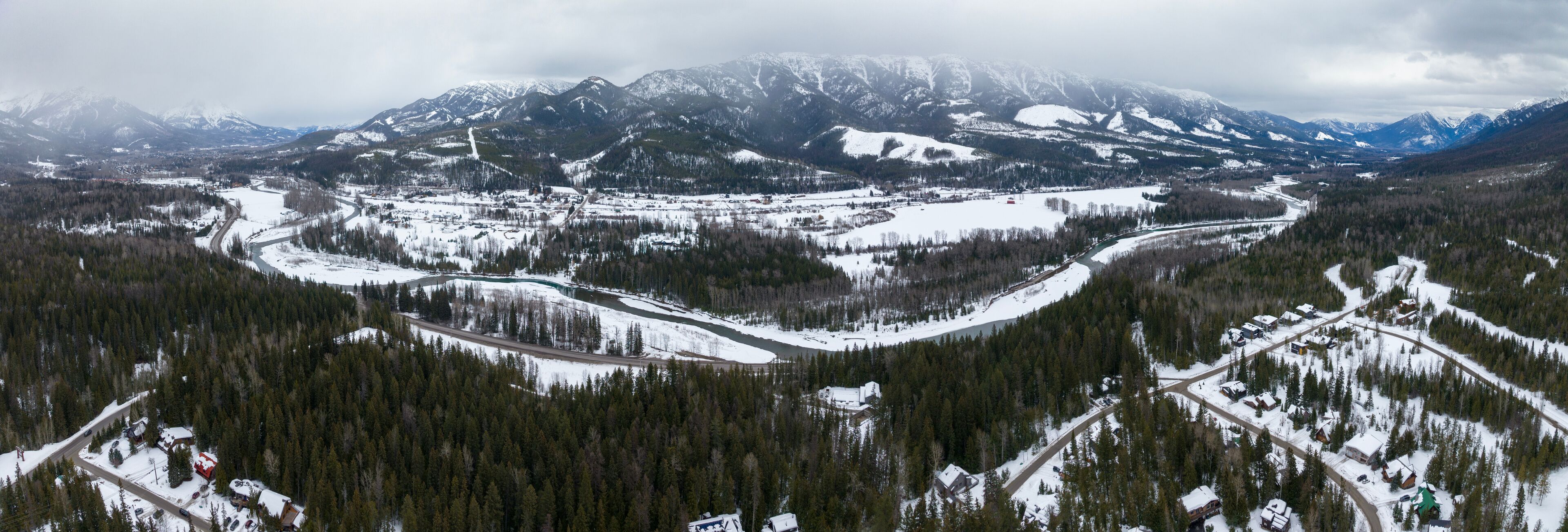 A snow-covered mountainous landscape with a river winding through a forested valley.