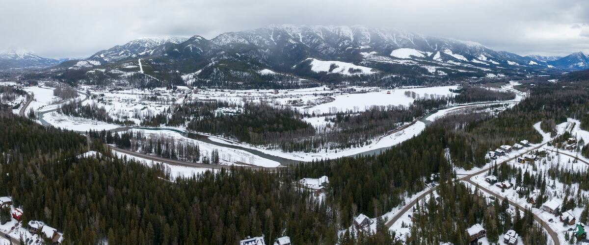 A snow-covered mountainous landscape with a river winding through a forested valley.