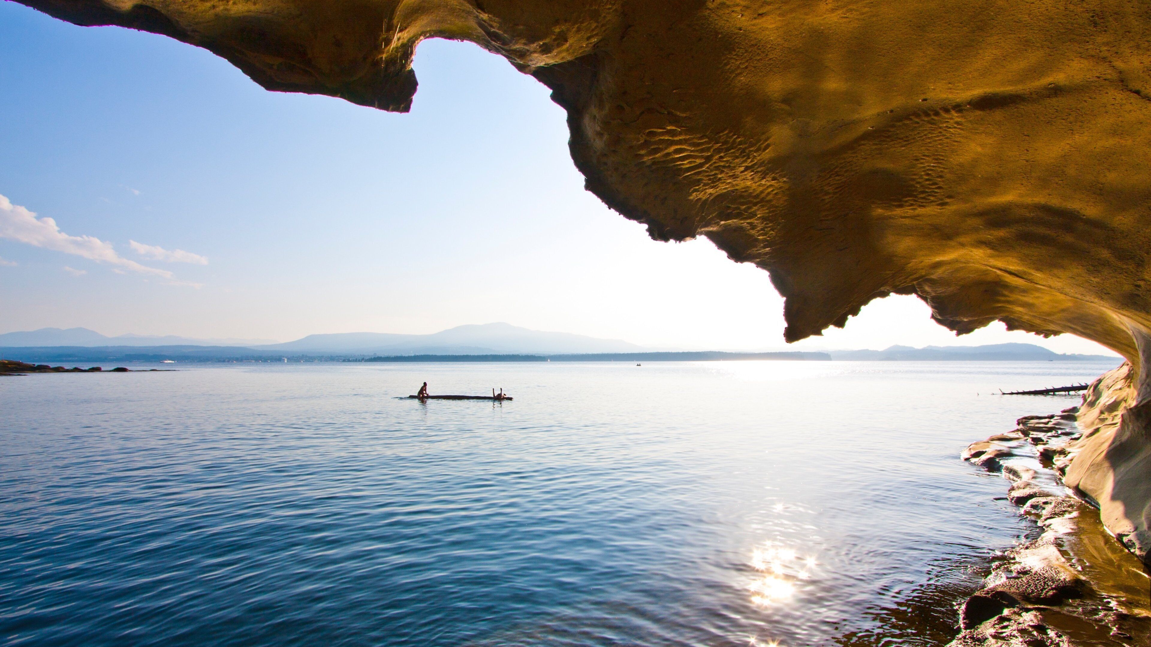 A calm lake with a person rowing a boat, surrounded by mountains and a rocky shoreline.