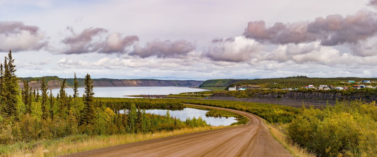 A dirt road curving through a landscape with a lake, forest, and a small settlement.
