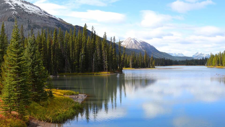 A calm lake surrounded by dense forests and snow-capped mountains.